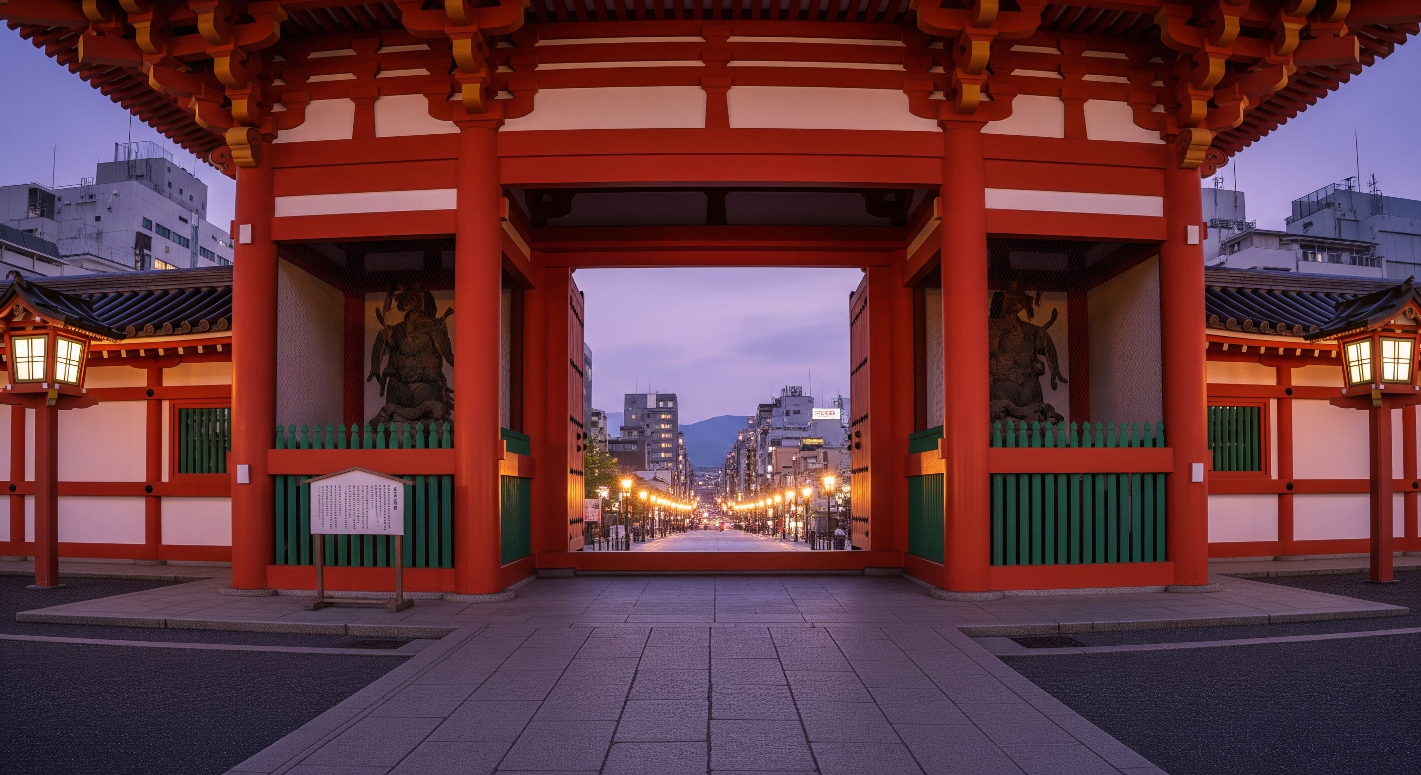 Yasaka Shrine vermilion nishi-romon gate at twilight with Shijo Avenue and city lights visible beyond, soft dusk sky