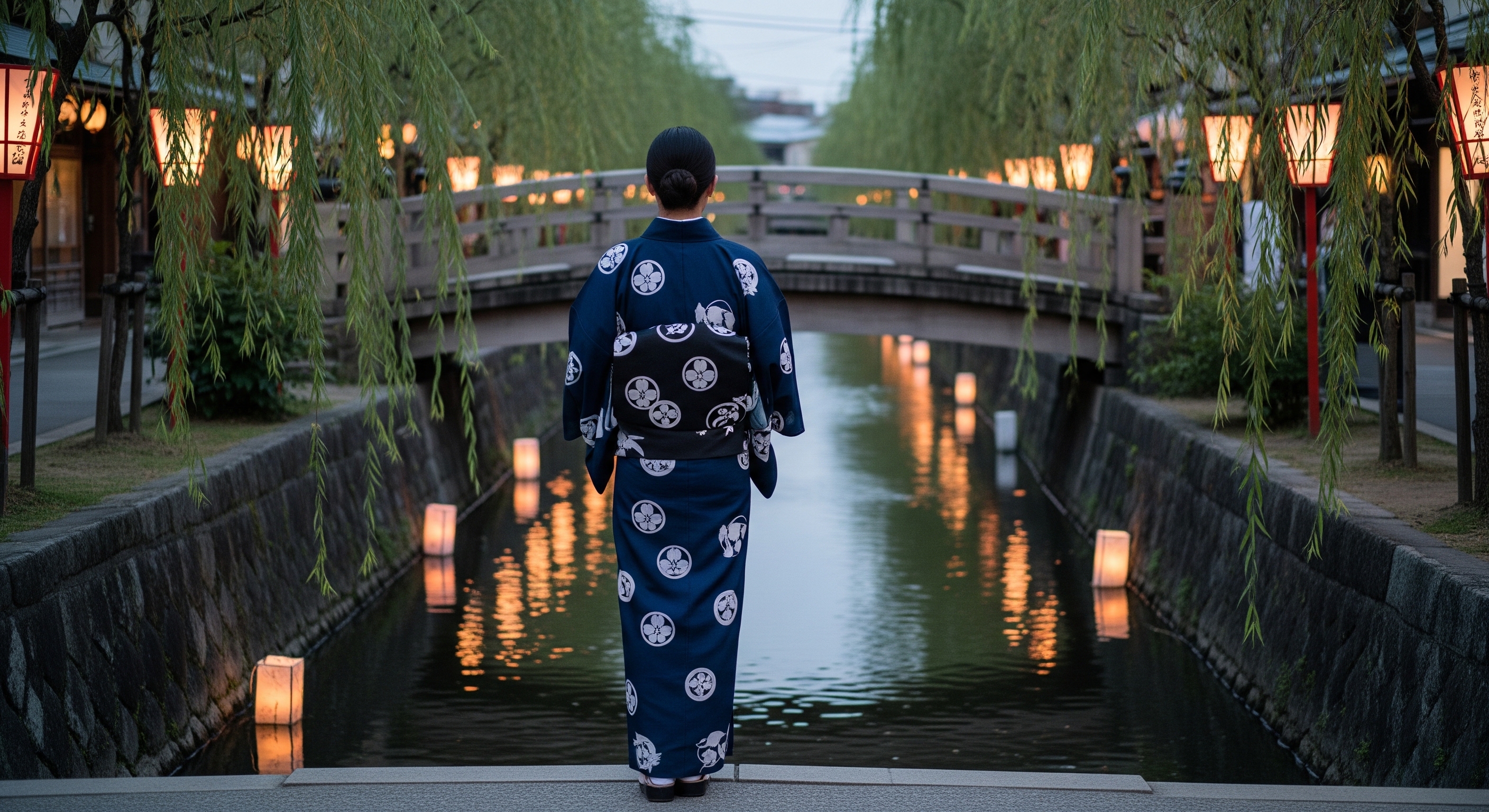 Person wearing a deep indigo kimono standing on a wooden bridge over the Shirakawa canal in Gion Shimbashi at dusk, paper lanterns glowing softly